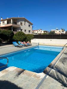 利马索尔EPISKOPI VILLA, Luxury 4 Bedroom with Pool - Limassol的一座游泳池,两位客人躺在大楼旁边的椅子上