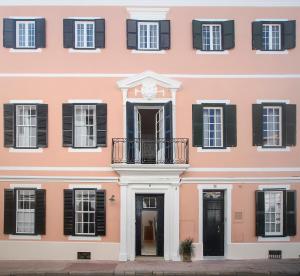 马翁Can Alberti 1740 Boutique Hotel的粉红色的建筑,设有黑色百叶窗和阳台