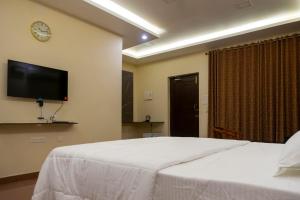 蓬蒂切里Pranaav Beach Resort的卧室配有白色的床和墙上的电视。
