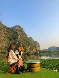 宁平Trang An Memory Homestay的两个女人坐在湖边的椅子上