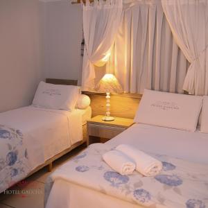 瓜伊拉Hotel Gaucha的客房设有两张床和一张带台灯的桌子。