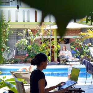 埃斯孔迪多港Casa Losodeli & Coworking- Adults Only的坐在桌边的女士,在游泳池边用笔记本电脑