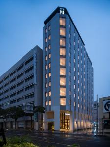 那霸Nest Hotel Naha Kumoji的一座高大的白色建筑,灯火通明
