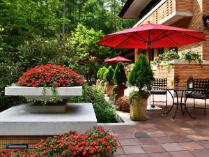 白马村Hotel La Neige的庭院配有带红色遮阳伞和鲜花的桌子