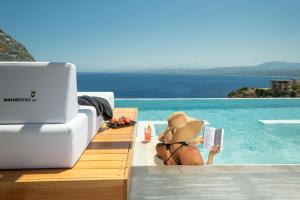 PalaiokastroMalvezzino Luxury Villas的戴帽子的女人在游泳池里读书