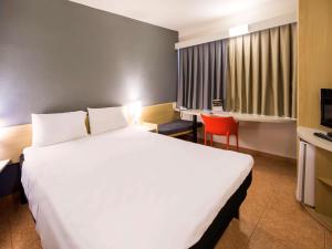 阿拉萨图巴ibis Araçatuba的酒店客房设有一张白色大床和红色椅子。