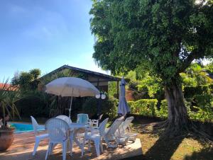 博伊图瓦Casa De Campo Boituva的一棵树旁边一群白色的椅子和一把伞