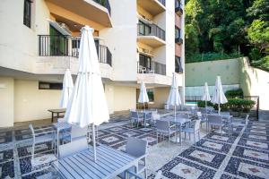里约热内卢Real Residence Hotel的庭院配有桌子、白色遮阳伞和椅子