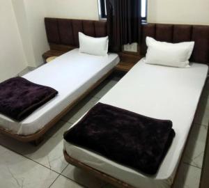 艾哈迈达巴德Hotel Milan的配有白色床单和棕色枕头的客房内的两张床