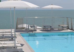 卡奥莱Hotel Marco Polo的毗邻大海的带椅子和遮阳伞的游泳池
