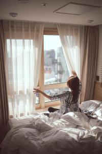 西归浦市Kenny Stay Jeju Seogwipo的坐在床上,从窗户望出去的女人