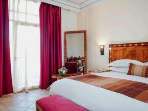 索维拉Hotel Le Médina Essaouira Thalassa sea & spa – Mgallery的一间卧室设有两张床、镜子和红色窗帘