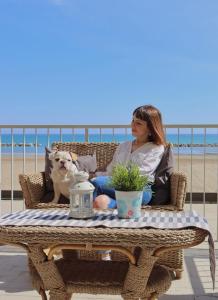 里米尼Nautic Beach Hotel的坐在椅子上的女人和狗一起坐在沙滩上