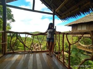 布桑加Sanctuaria Treehouses Busuanga的站在木制阳台上的妇女,享有森林美景