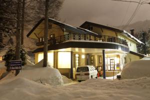 白马村K's House Hakuba Alps - Travelers Hostel的雪中的房子,前面有停车位