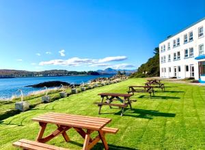 洛哈尔什教区凯尔高地Lochalsh Hotel with Views to the beautiful Isle of Skye的水边草上一排野餐桌