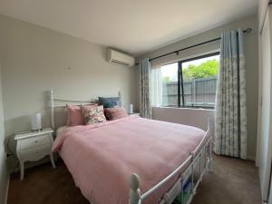 奥克兰Auckland Cornwall Park holiday Home的一间卧室配有一张带粉色床单的床和一扇窗户。
