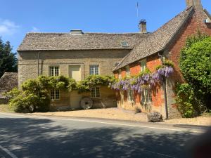 BledingtonStable Lodge at Bledington Mill的一座古老的砖房,上面有紫色花圈