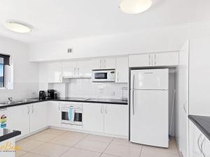 浅滩湾Breakwater Apartment 402的厨房配有白色橱柜和冰箱。