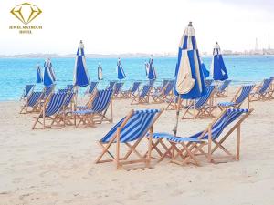 马特鲁港Jewel Matrouh Hotel的海滩上的蓝色椅子和遮阳伞