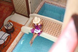 马拉喀什Riad Sidi Mimoune & Spa的坐在游泳池的戴帽子的女人