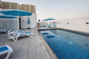 迪拜City Avenue Al Reqqa Hotel的一座带椅子和遮阳伞的游泳池位于一座建筑旁边