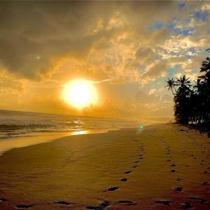 希克杜沃Mirage Beach House at Morava Court的沙滩上的日落,沙滩上留下了脚印