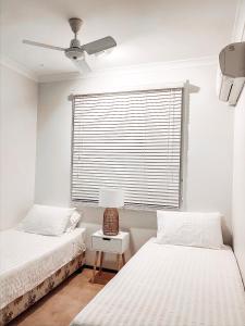 卡那封Carnarvon 3BR & 2BA Holiday House的一间卧室设有两张床和一个带风扇的窗户。