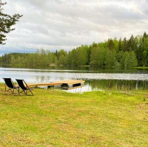 TromsiSaarjärve Puhkemaja Glämping的两把椅子坐在湖边码头附近的草地上