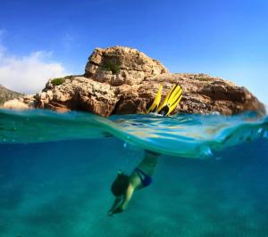 坎布里尔斯Casa bonmont con vistas al mar piscina y port aventura的一个人在海洋岩石附近的水中游泳