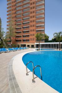 贝尼多姆Aparthotel BCL Levante Lux的一座带椅子的游泳池,一座高高的建筑