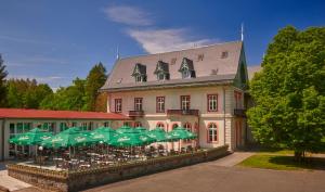 赫任斯科Hotel Mezní Louka的前面有桌子和绿色遮阳伞的建筑