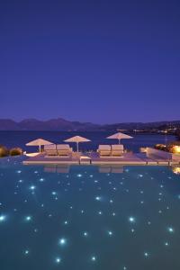 阿基欧斯尼古拉斯The Island Concept Luxury Boutique Hotel Heated Pool的游泳池在晚上提供椅子和遮阳伞