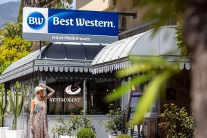芒通Best Western Hotel Mediterranee Menton的站在建筑物前身穿衣服的女人