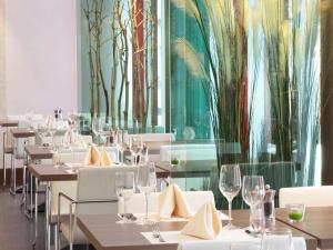 林茨林茨宜必思尚品酒店的餐厅墙上挂着白色桌椅和树木