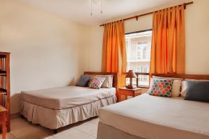 南圣胡安Hostel Tropical and CoWorking的配有橙色窗帘和窗户的客房内的两张床