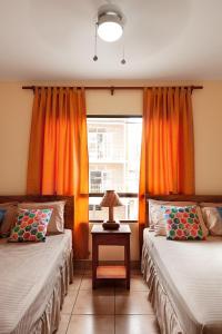 南圣胡安Hostel Tropical and CoWorking的客房设有两张床和一个带橙色窗帘的窗户。