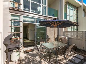 陶波24 Marina View Retreat - Taupo Holiday Apartment的一个带玻璃桌和遮阳伞的庭院