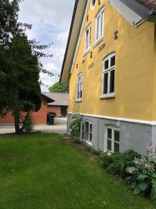 欧登塞Allesø Gl. sognefoged gård的黄色的建筑,设有窗户和绿色的院子