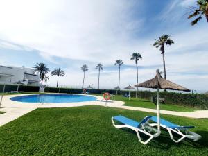 卡博皮诺Marbellamar Seaviews的一个带两把椅子和一把遮阳伞的游泳池,并种植了棕榈树