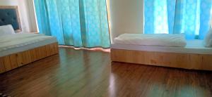 列城Zee Guest House的客房内设有两张床,铺有木地板,配有蓝色窗帘。