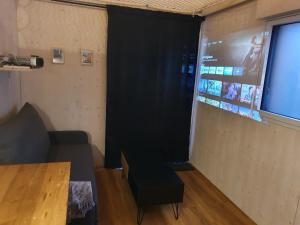 昂热TINY HOUSE Cosy 1 - Angers Green Lodge的一间设有黑色窗帘、沙发和屏幕的房间