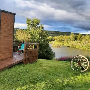 AðaldalurHagi 1 Guesthouse的河边草地上的木甲板,配有椅子