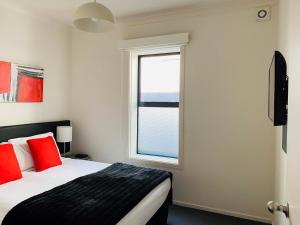 但尼丁315欧式汽车旅馆及服务公寓的一间卧室配有一张带红色枕头的床和一扇窗户