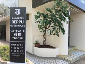 别府J-Hoppers Beppu Guesthouse ジェイホッパーズ別府ゲストハウス的建筑物前有标志的树