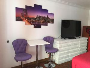 南旧金山阿美莉卡那汽车旅馆的一间设有两张紫色椅子、一张桌子和一台电视的房间