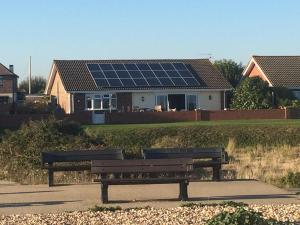 帕格汉姆Pagham Getaways的两把公园长椅,位于一栋带太阳能电池板的房屋前