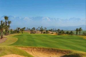 马拉喀什Cosy Loft Emeraude Marrakech Prestigia Golf City的一座棕榈树和山脉环绕的高尔夫球场