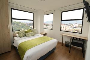 波哥大Normandía Tower的一间卧室配有一张床、一张书桌和三扇窗户。