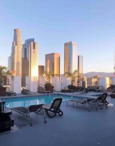 洛杉矶Huge Downtown LA Loft with Rooftop Pool & Jacuzzi的一个带椅子的游泳池,并拥有城市天际线的背景